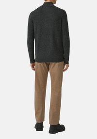 Dunkelgrauer Strickpullover mit hohem Kragen, kombiniert mit hellbrauner Hose und schwarzen Schuhen. Verfügt über gerippte Bündchen und Saum.