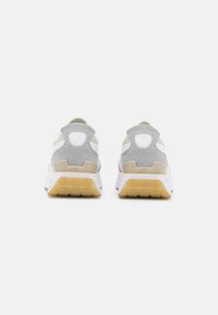 Paire de baskets Puma grises et beiges avec semelles intermédiaires blanches et semelles extérieures translucides en gomme vues de dos.