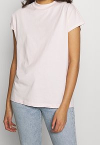 Ljusrosa t-shirt med kort ärm i mjukt bomullstyg. Har rund halsringning och avslappnad passform, kombinerad med ljusblå jeans.