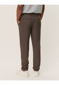 Brune bukser med houndstooth-mønster og straight-leg pasform, med baglommer og en blød tekstur, parret med hvide sneakers.
