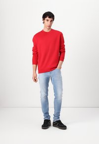 Rød sweatshirt med lange ærmer, rund halsudskæring og lille logo. Kombineret med lyseblå jeans og sorte sneakers. Enkel design, afslappet pasform.