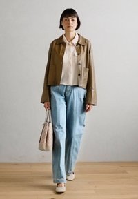 Veste en cuir marron courte sur un chemisier blanc, jean taille haute bleu clair, chaussures claires et sac à main à motifs roses.