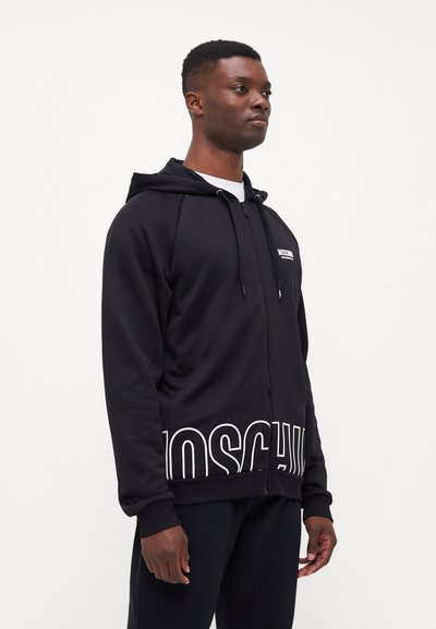 Black zip-up hoodie made of soft fabric, featuring a white logo on the chest and large text at the hem, with a relaxed fit and hood.
