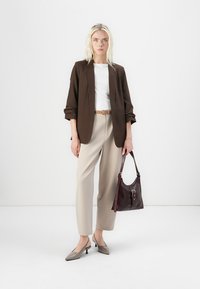 Hnedý blazer cez bielu košeľu, béžové nohavice a šedé lodičky. K outfitu patrí tmavo burgundská taška so strieborným zapínaním.