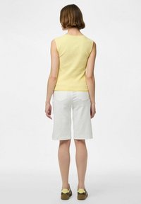 Ljusgul, randig ärmlös topp i kombination med vita knälånga shorts, med vågformad nederkant och bakfickor. Bruna och gula skor.