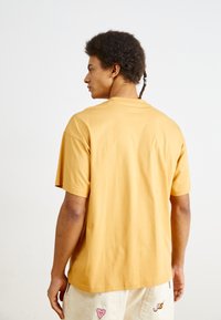Tricou cu mânecă scurtă de culoare galben muștar, confecționat din bumbac moale, cu o croială relaxată și un decolteu rotund, văzut din spate.