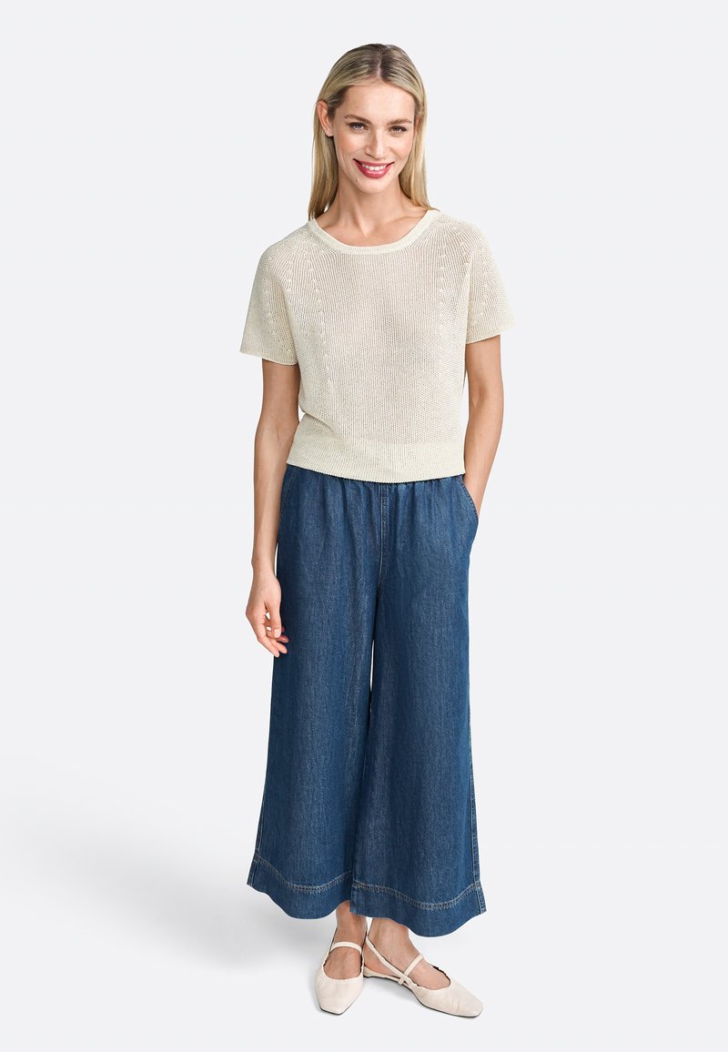 Top de punto color beige claro combinado con culottes amplios de mezclilla oscura y bailarinas beige. El top tiene mangas cortas y un escote redondo.