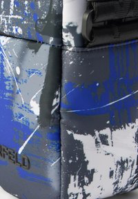 Γκρι και μπλε τυπωμένο υφασμάτινο τσάντα με υφή, με αφηρημένο σχέδιο νερομπογιάς και εμφανές μαύρο λογότυπο.