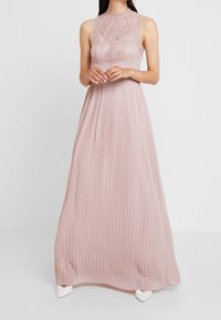 Fijnroze maxi-jurk met geplooide rok, kanten lijfje met ingewikkelde patronen, ronde halslijn en mouwloos ontwerp.