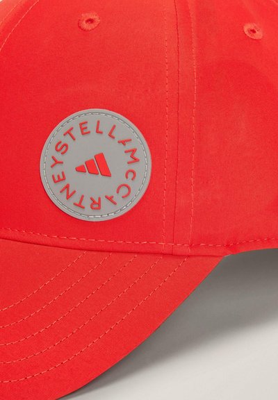 Gorra de béisbol roja con visera bordada, que presenta un parche de logo gris circular con texto en relieve y un diseño gráfico triangular.
