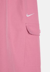 Ružový odev s klopovou kapsou a strieborným logom Nike Swoosh. Vyrobený z hladkej textúrovanej tkaniny s viditeľnými švou.