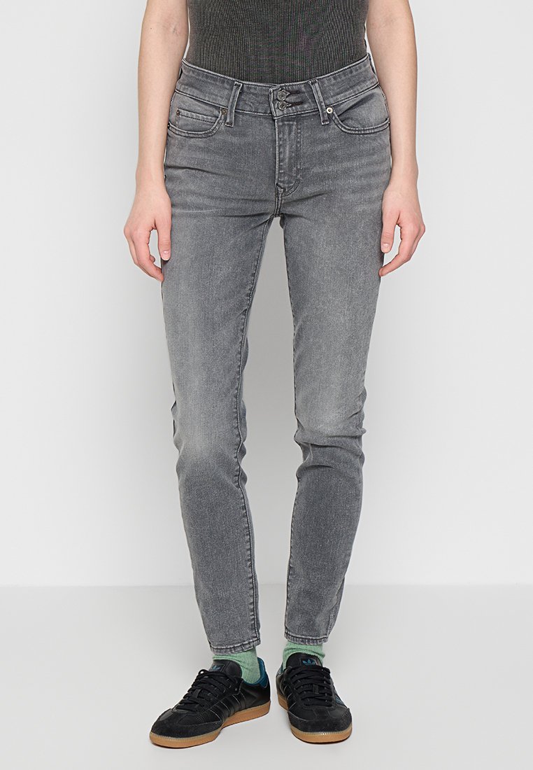 Vaqueros skinny grises con un acabado desgastado, cinco bolsillos, trabillas para el cinturón y cierre de cremallera. Combinados con zapatillas negras y calcetines verdes.
