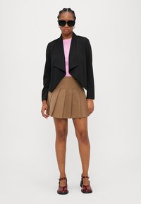 Fekete cropped dzseki redőzött elülső résszel, rózsaszín testhezálló top és khaki redőzött szoknya. Fekete és burgundi cipővel kiegészítve.