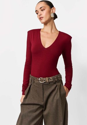 Bordowy, długorękawkowy body z głębokim dekoltem w serek. Połączony z brązowymi, plisowanymi spodniami z wysokim stanem oraz paskiem w panterkę z srebrną klamrą.