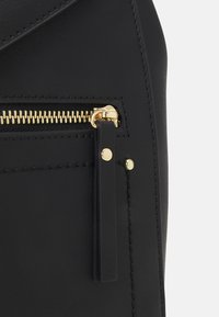Black leather bag featuring a gold zipper with a contrast stitch and a leather zipper pull tab. Smooth texture with sleek design.