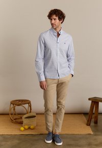 Lichtblauw overhemdd met een geometrisch patroon, gecombineerd met beige chino's en grijze schoenen. Soepele stof, slim fit en subtiele branding.