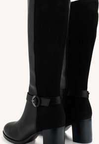 Botas negras hasta la rodilla que combinan cuero liso y ante. Tacón alto grueso, cremallera lateral y un toque decorativo de hebilla.