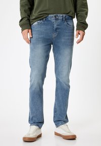 Lyseblå denimjeans med lige snit, der har et klassisk fem-lommers design og diskrete slidmærker. Bæres med hvide sneakers.