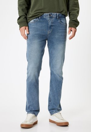 Lyseblå denimjeans med lige snit, der har et klassisk fem-lommers design og diskrete slidmærker. Bæres med hvide sneakers.