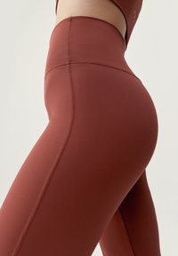 Vysoké športové legíny v tmavočervenej farbe, vyrobené z hladkej, elastickej látky. Obsahujú kontúrovaný šev pre lepšie prispôsobenie.