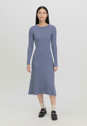 Rippstrickkleid in Hellblau, lange Ärmel, taillierter Oberteil, ausgestellter Rock, weiche Textur. Kombiniert mit schwarzen Slippern und hellen Socken.