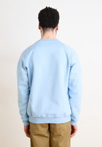 Ljusblå sweatshirt med rund hals och raglanärmar, med en mjuk textur och ribbade ärmslut, parat med khakibyxor.