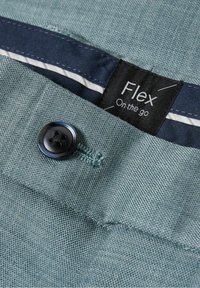 Tissu bleu sarcelle avec une finition texturée, doté d'un bouton noir et d'une étiquette indiquant "Flex On the go" derrière une doublure rayée bleu marine et blanche.