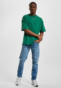 Grønn bomull t-skjorte med korte ermer, kombinert med lyseblå denimjeans. Utseendet fullføres med hvite sneakers og et sølvkjede.