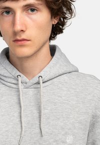 Sivá mikina s kapucňou na šnúrku, vyrobená z textúrovaného materiálu s vyšívaným logom na hrudi. Mäkka a ležérna konštrukcia.