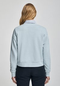 Ljusblå kort sweatshirt med mjuk textur, rund halsringning och sänkta axlar. Har ribbade muddar och nederkant.