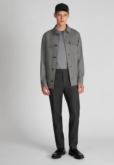Graue button-up Jacke über einem grauen T-Shirt, kombiniert mit dunkelgrauen Hosen und schwarzen Schuhen. Die Jacke verfügt über zwei Brusttaschen und einen Kragen.