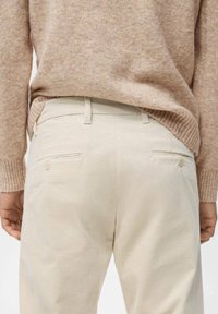 Pantalones de pana color crema con bolsillos traseros. Llevados con un suéter de textura marrón claro. Enfocado en el patrón acanalado y los tonos neutros.