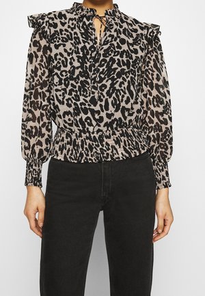 Femme portant un chemisier à manches longues à imprimé léopard avec des épaules à volants et un col noué, associé à un pantalon noir taille haute.