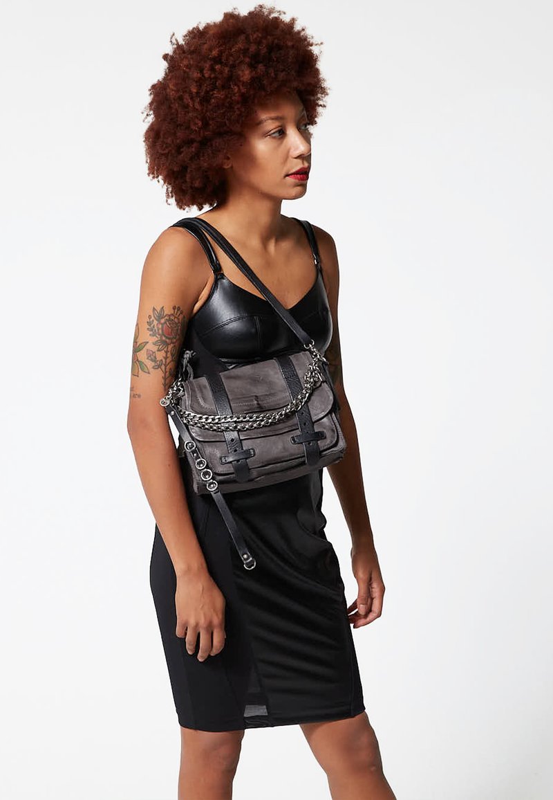 Grijze schoudertas met een gestructureerde afwerking, voorzien van een zilveren kettinkje en zwarte accenten. Compacte rechthoekige vorm met verstelbare bandjes.