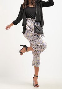 Černý otevřený kardigan přes černý top, spárovaný s kalhotami v pastelových vzorech a černými sandály na vysokém podpatku. Malá černá kabelka přes rameno.