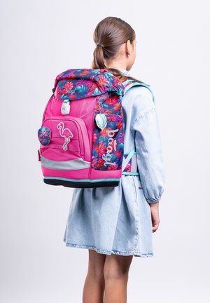 Kind trägt einen rosa und blumigen Rucksack mit Flamingo-Aufnäher und Accessoires, angezogen in einem hellblauen Jeanskleid, blickt nach hinten.