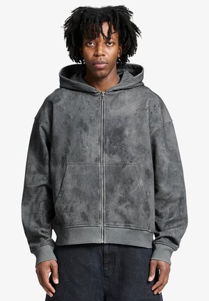 Felpa grigia con zip in tessuto testurizzato, dotata di tasca frontale e cappuccio con coulisse. Vestibilità rilassata con polsini e orlo a costine.