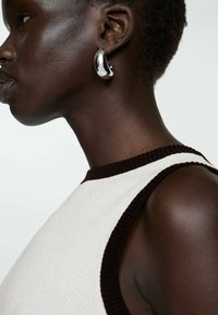 Black sleeveless top with contrasting brown ribbed neckline. Model wearing shiny metallic hoop earring, close-up profile view.
