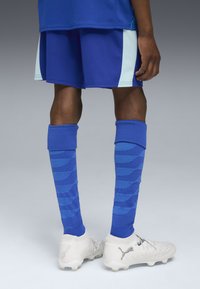 Zils sporta krekls un šorti, ko papildina zila līdz ceļiem augsta zeķes ar viļņu rakstu. Balti sporta apavi ar sudraba akcentiem noslēdz izskatu.