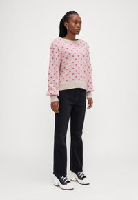Lyserød sweater med mørkerøde prikker, ribbet halsudskæring og manchetter. Sammen med sorte jeans og hvide platåsneakers med sorte detaljer.