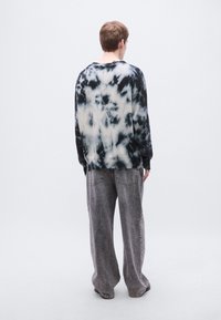 Μαύρο και λευκό φούτερ με σχέδιο tie-dye, χαλαρή εφαρμογή, στρογγυλή λαιμόκοψη και μακριά μανίκια, συνδυασμένο με γκρι τζιν παντελόνι φαρδιάς γραμμής.