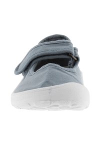 Zapato de tela gris con una amplia correa de velcro, puntera redondeada y suela blanca de goma. Presenta una textura suave y un diseño casual para un uso fácil.