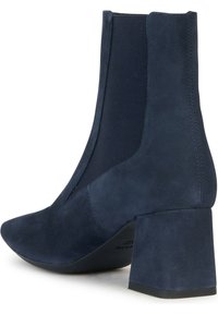 Stivale alla caviglia in suede blu navy con punta affusolata, pannelli laterali elasticizzati e tacco bloccato spesso. Texture liscia, linee pulite e nessuna ferramenta visibile.