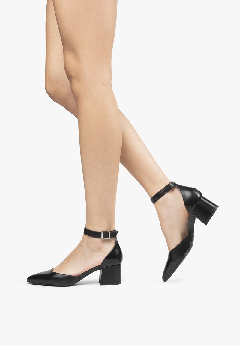 Scarpe pump in pelle nera con punta affusolata, cinturino alla caviglia e tacco a blocco. La texture liscia e il design minimalista accentuano l'eleganza.