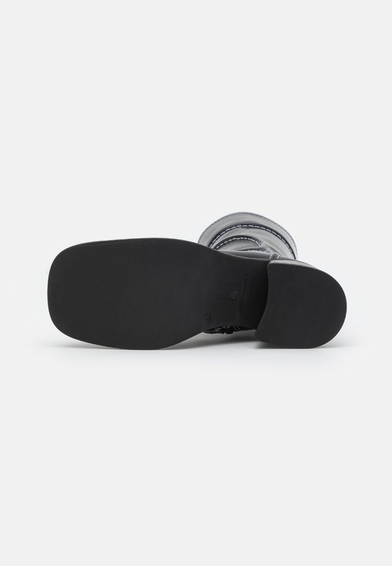 Zwarte rubberen outsole van een laars met een gestructureerd oppervlak. Heeft een gladde, ronde vorm en een minimaal loopvlakpatroon.