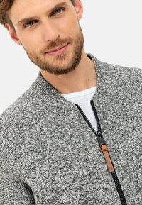 Graue gemusterte Bomberjacke mit strukturiertem Strick, Rundhalsausschnitt, Frontreißverschluss und braunem Akzent am Reißverschluss-Schieber.