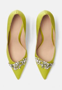 Zelene satenske balerinke s šiljastim vrhom i ukrasom od dragulja na prstima. Glatka tekstura i nisko rezane strane poboljšavaju dizajn.