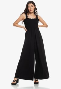 Black, sleeveless jumpsuit with a smocked bodice; wide-leg design; soft, stretchy fabric; scalloped edges at the neckline; ankle-height.