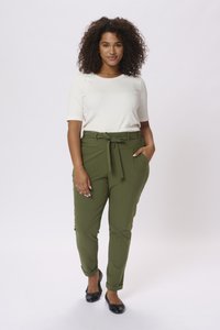 Pantalons pieds de poule verts olive avec taille nouée, coupe fuselée et poches sur les côtés, associés à un haut blanc à manches courtes et des ballerines noires.