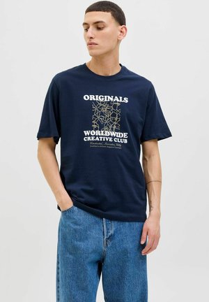 Camiseta de algodón azul marino con un diseño gráfico blanco y dorado con texto. Corte relajado, mangas cortas, combinada con pantalones de mezclilla azules.
